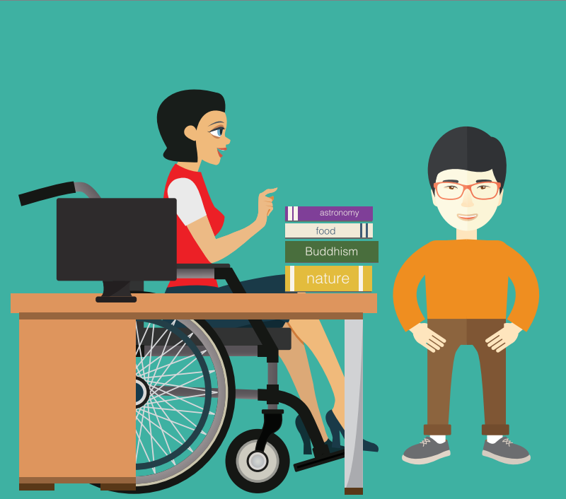 A boy stands to the right of a stack of books sitting on a desk with a computer. A woman in a wheelchair sits at the desk.