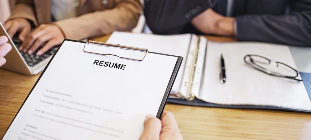An individual holding a resume before two other business individuals.