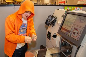 A young man wearing a hoodie is seen collecting change from a grocery store self-check machine.