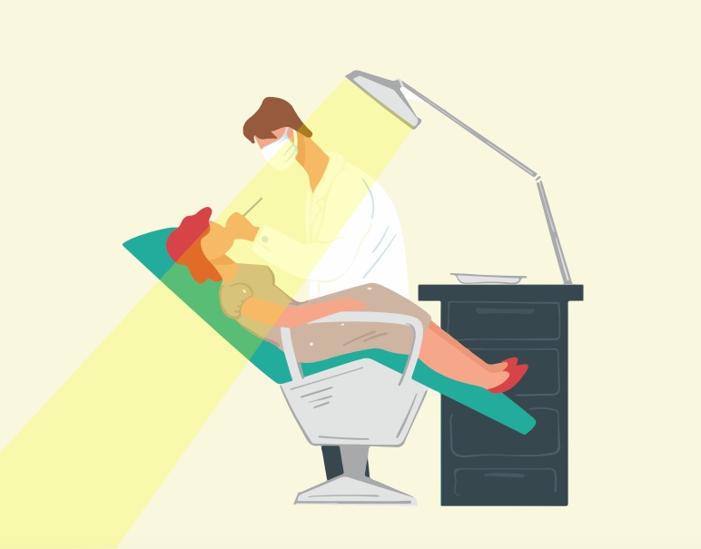 A boy sitting in a dentist's chair while a dentist shines a light on his teeth.
