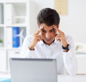 Picture of a man working on his computer, he looks stressed. 