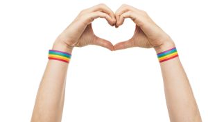 LGBTQ+, same-sex love and homosexual relationships concept - close up of male hands with gay pride rainbow awareness wristbands showing heart gesture